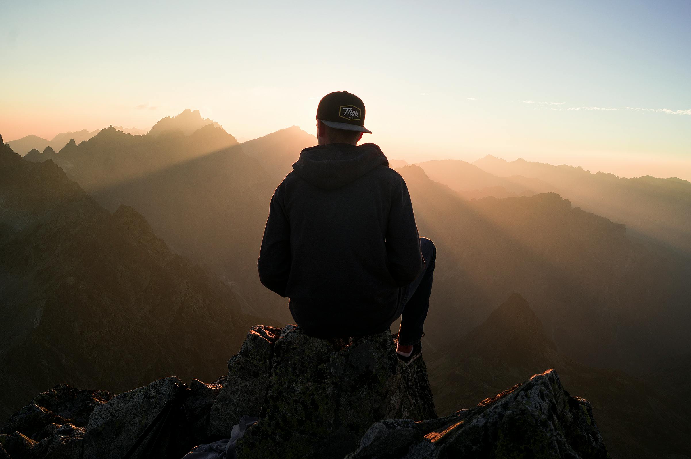man sitting on the top of the mountain watching the sunset from high in the sky